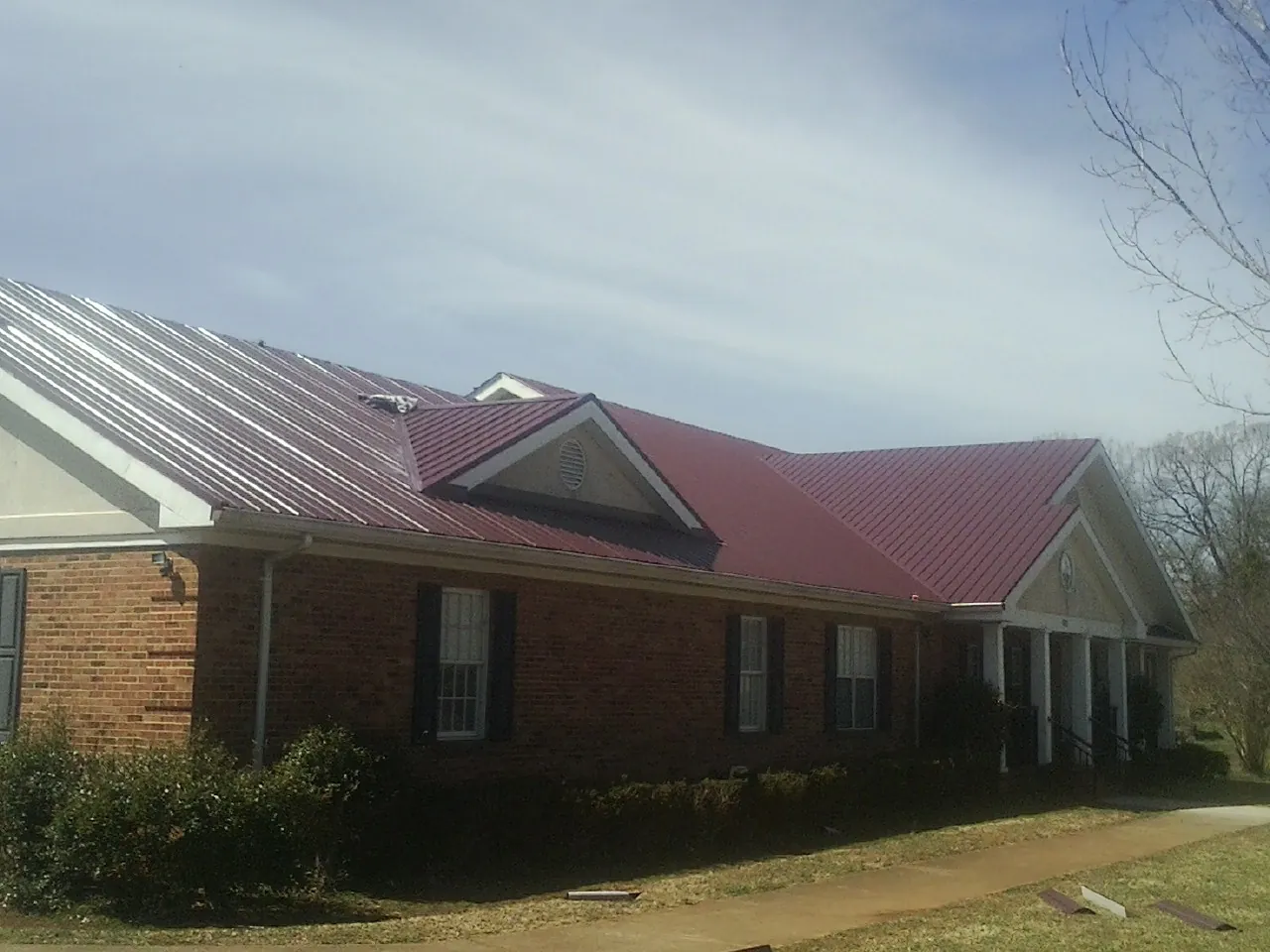 Red metal roof with gabled entries on a long brick building, from a Hail Damage Roof Repair job in Boligee