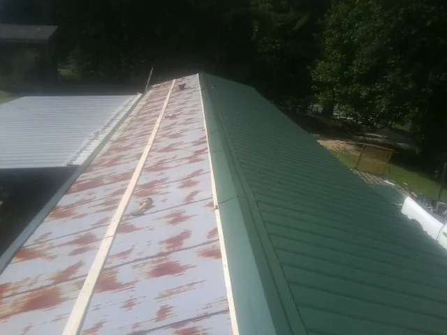 Old rusted panels beside newly installed green metal roofing — Wind Damage Roof Repair by Roofing Brothers in Boligee