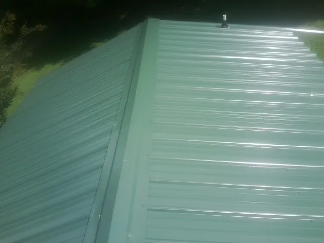 New green metal panels meeting at the ridge of a roof — Flat Roof Repair work by our crew in Boligee