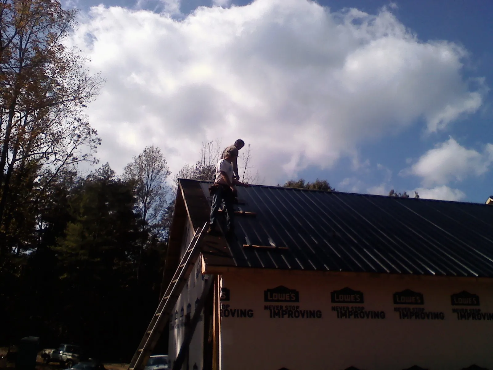 Roofer fastening dark metal panels high against a cloudy sky, from a Roof Inspection job in Boligee