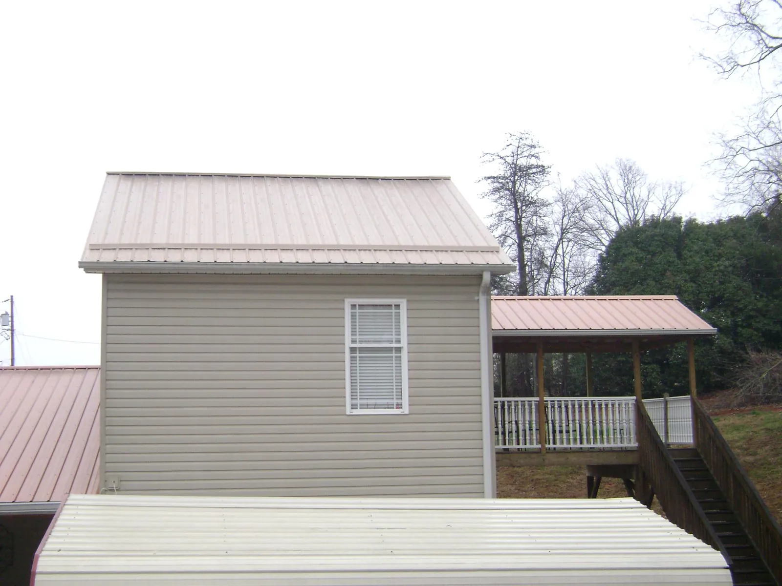 Tan metal roofs on a two story addition and attached porch, from a Roof Replacement job in Boligee